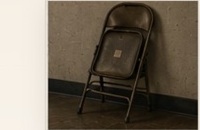A folded black chair leaning against a rehearsal-room wall.