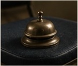 A brass desk bell resting on a black folding chair.